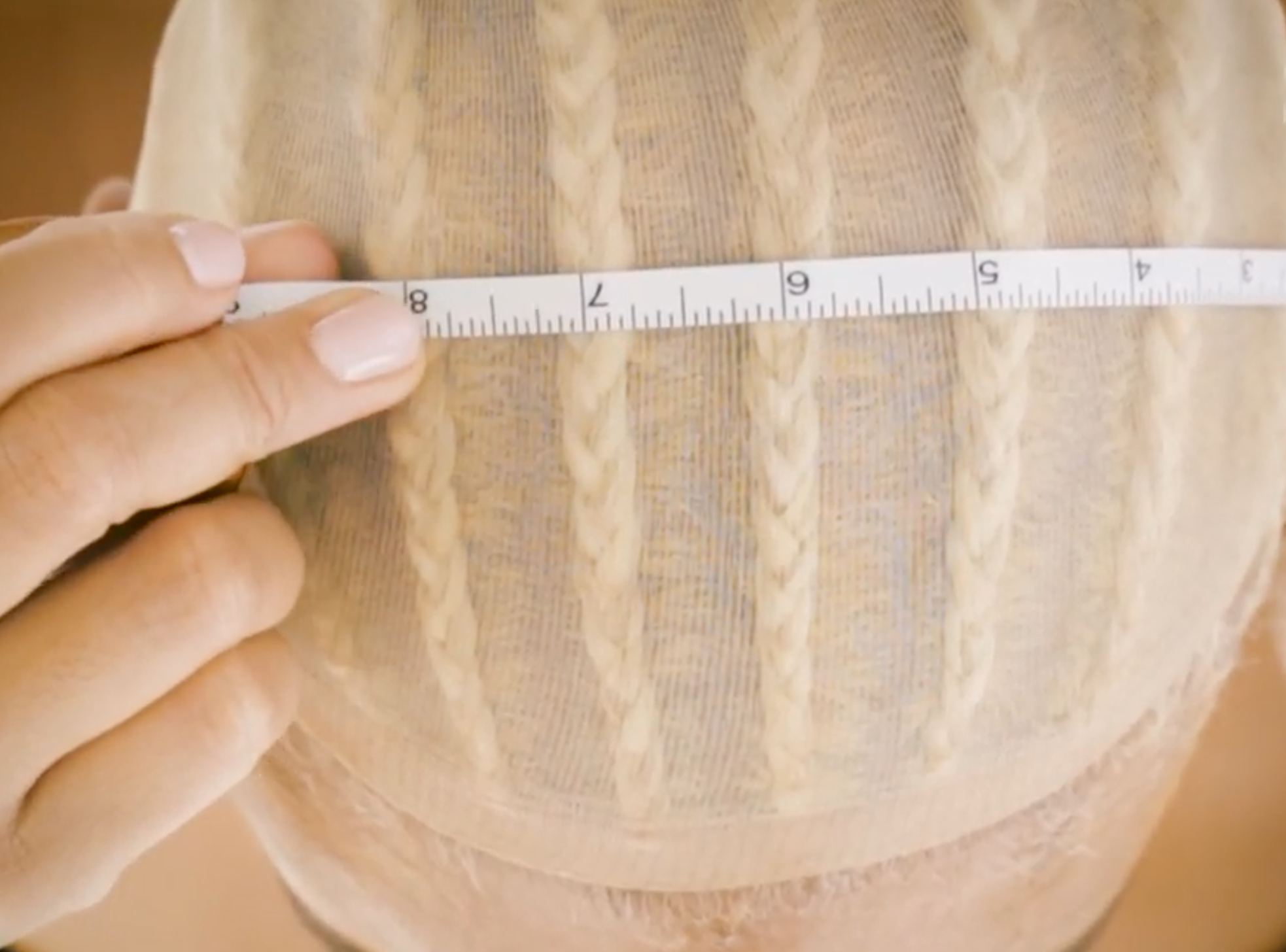 Woman with wig cap on measuring her head from ear to ear.